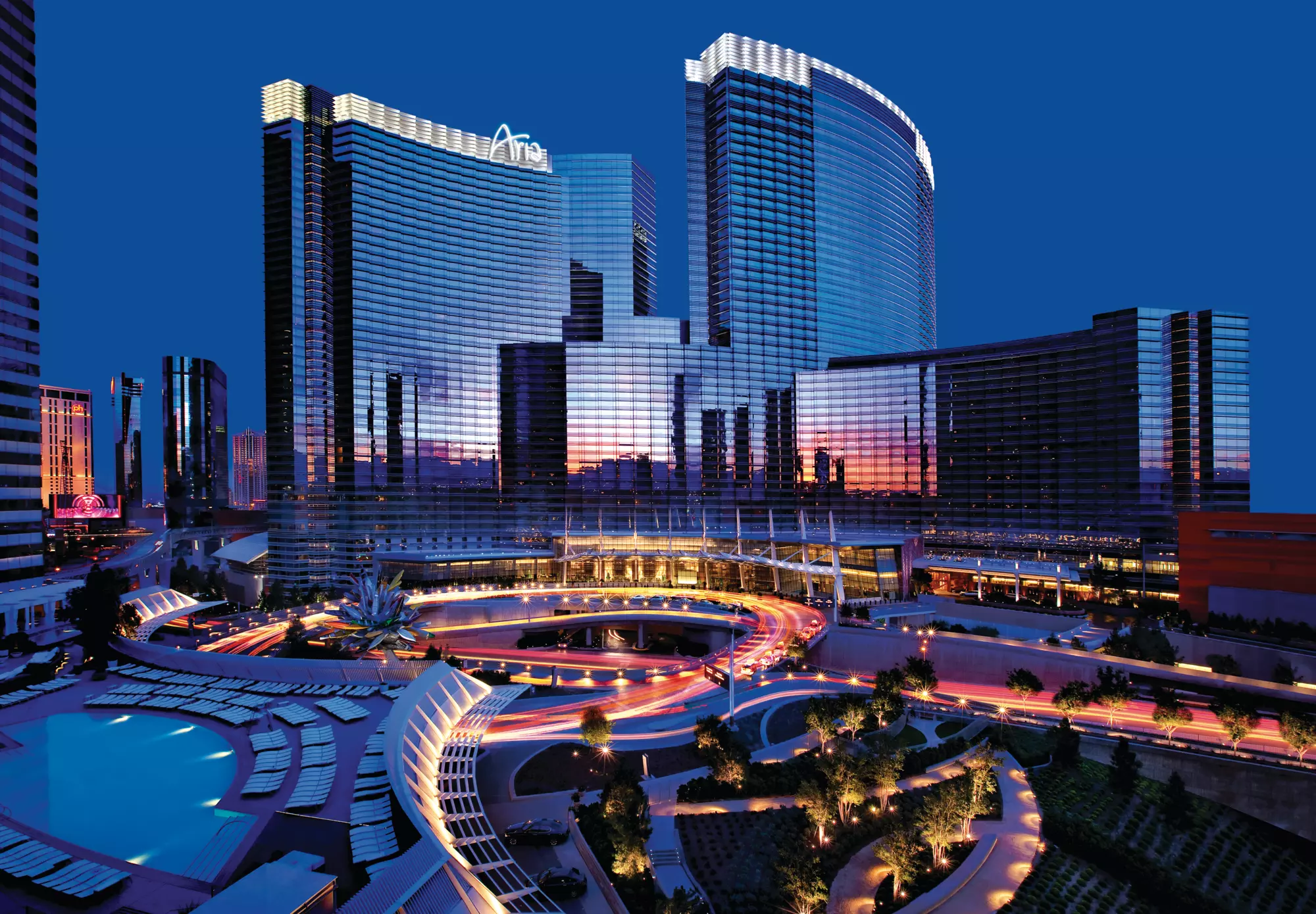 A photo of the Aria Hotel, several tall mirrored buildings with a pool and pathways lit up in front, at night..