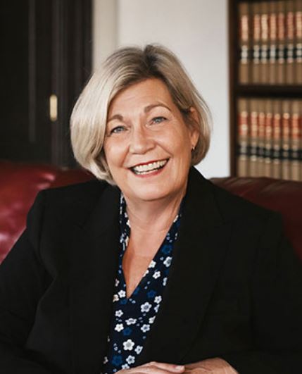 Betsy Green in a dark suit sitting in front of a bookcase.